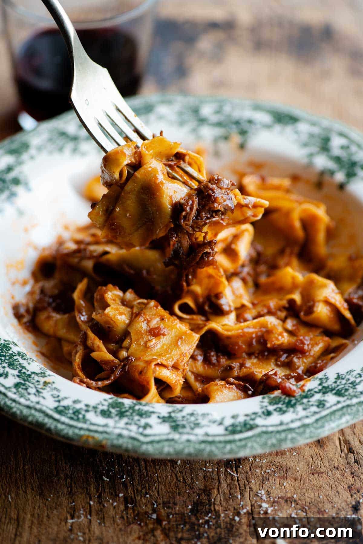 A side shot of a fork picking up some beef ragu and pappardelle pasta, showcasing the perfect cling of sauce to pasta.