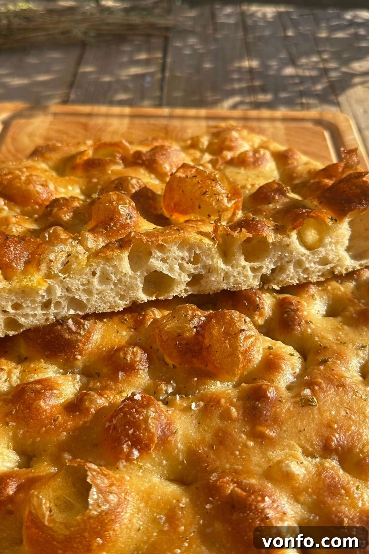 Snooze Button Overnight Focaccia 7 A golden and airy focaccia cut in half to show it's bubbly texture sitting on a wooden chopping board.