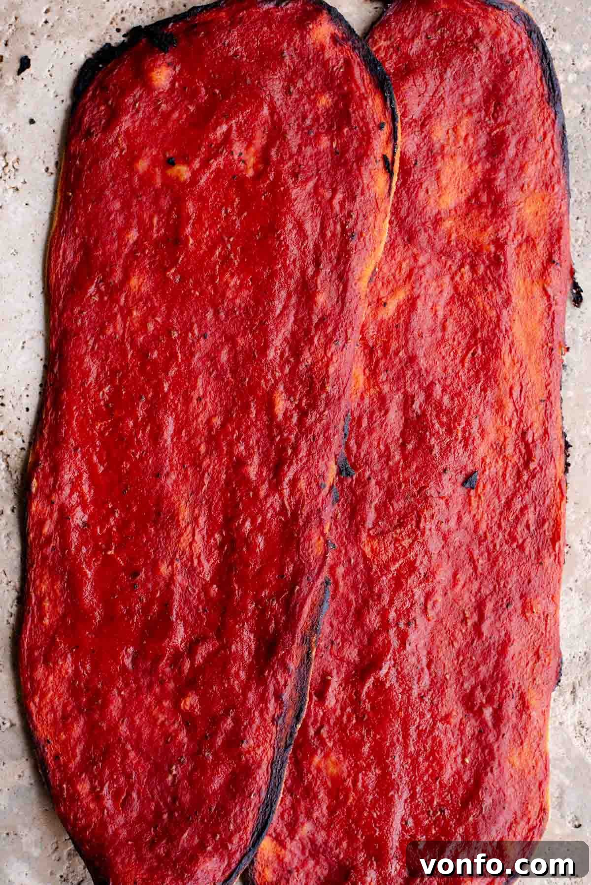 Fast & Crispy Pizza Fingers 2 Two long thin and crispy pizzas covered in tomato sauce sitting on a travertine surface.
