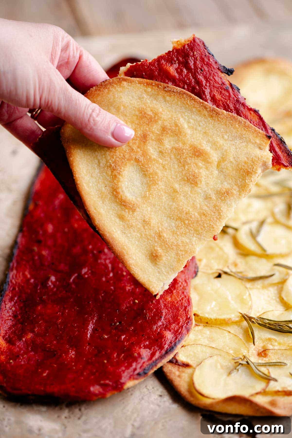 Fast & Crispy Pizza Fingers 7 A hand holding a thin and crispy pizza folded in half covered in tomato.