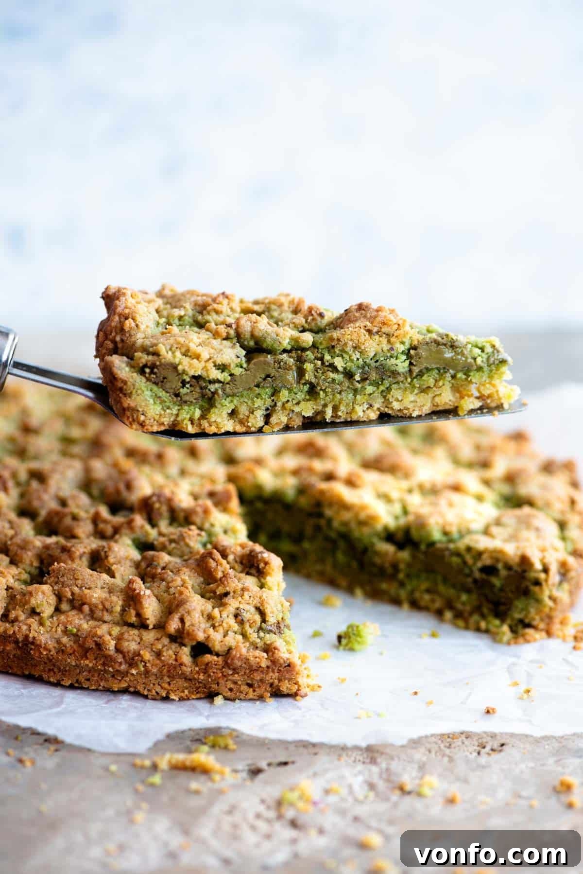 Rustic Italian Pistachio Crumb Cake 2 A cake server holding a slice of pistachio crumb cake, revealing a vibrant layer of pistachio cream in the middle.