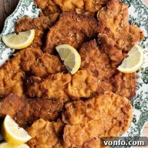 A close-up of breaded pork cutlets on a serving plate with lemon wedges, showcasing their crispy texture.