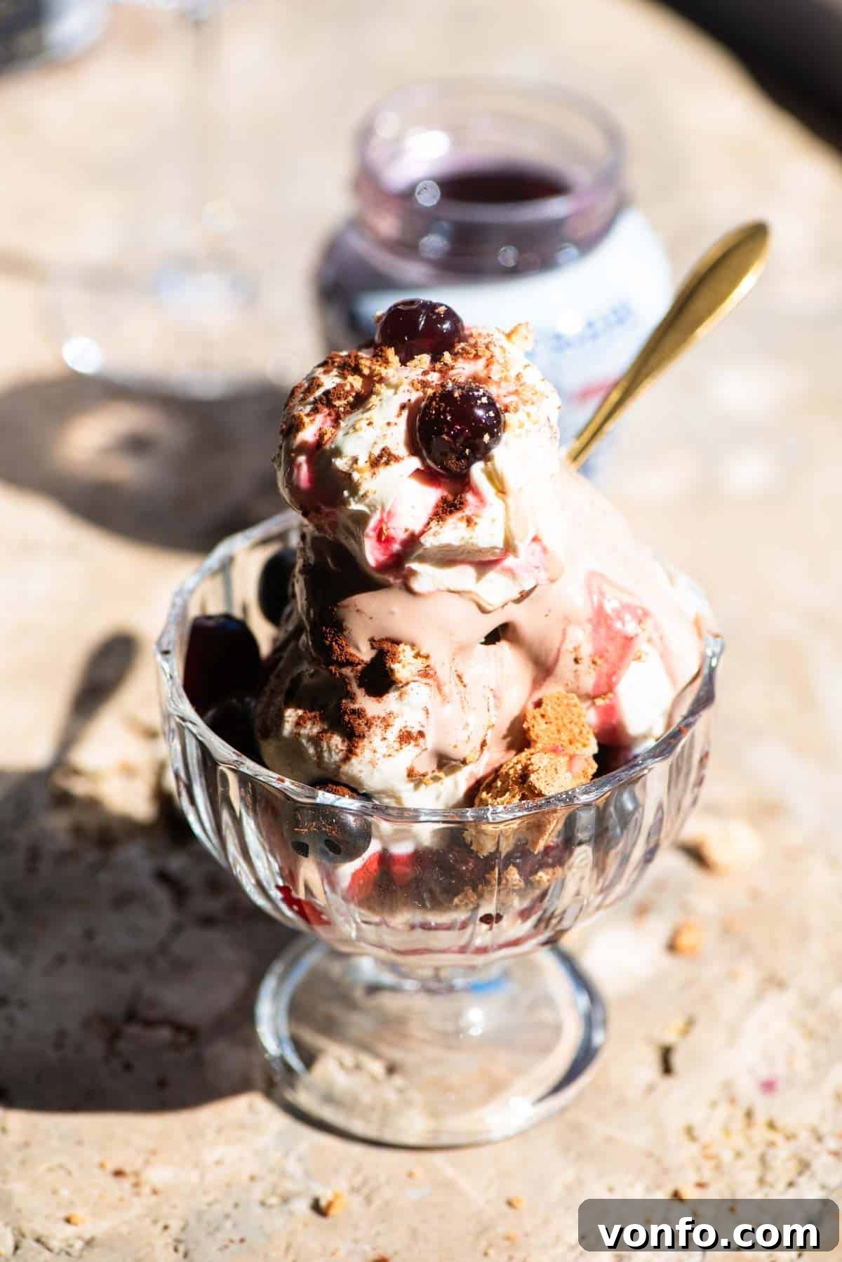 An Italian ice cream sundae in a glass bowl with cream and cherries on top sitting on a travertine surface.