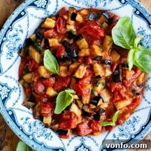 Golden Fried Eggplant Simmered in Rustic Tomato Sauce 5 A close up of fried eggplant in a cherry tomato and basil sauce. It's presented in a blue and white country style bowl.