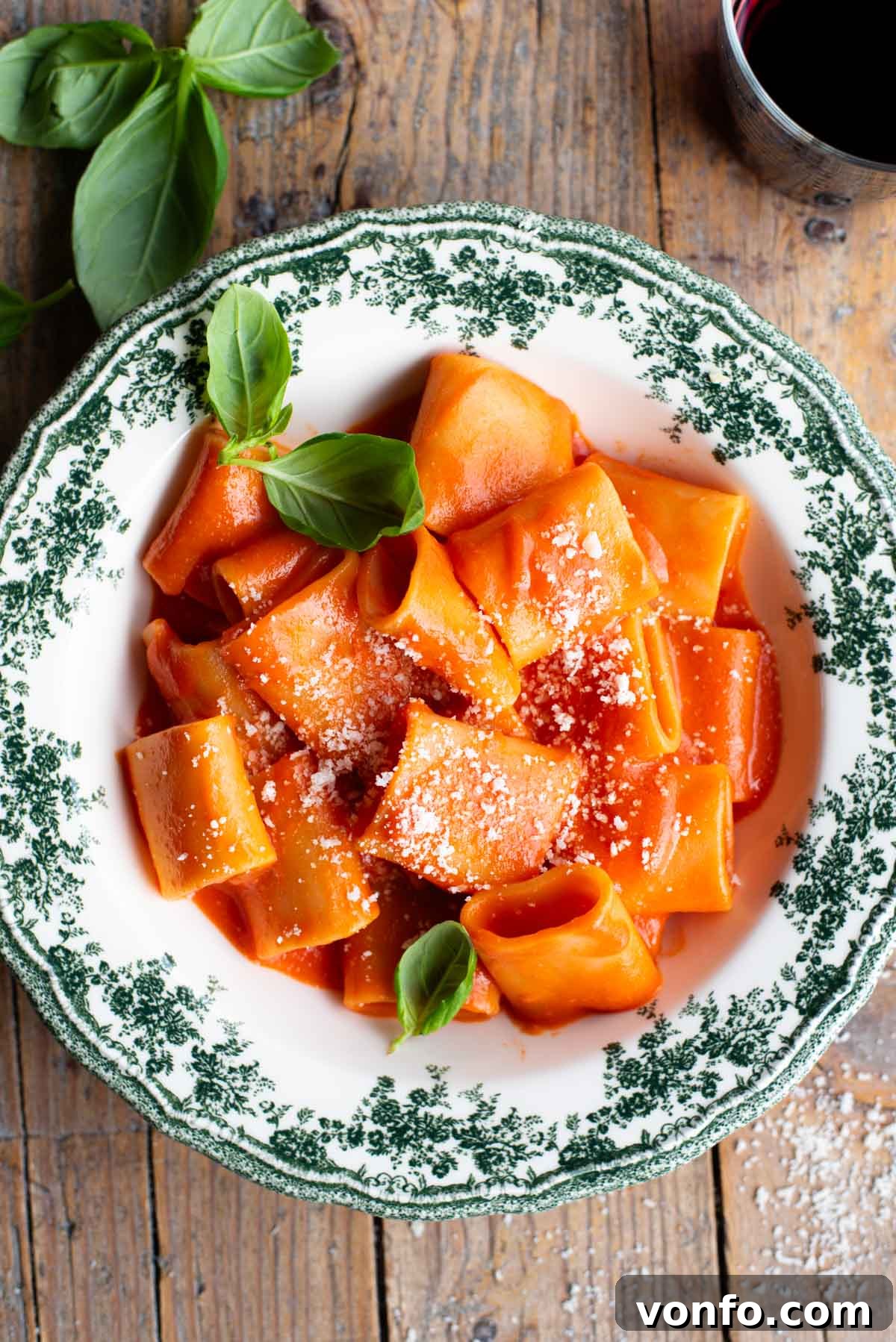 Paccheri pasta with a smooth tomato sauce in a green and white patterned bowl topped with basil, ready to be served.