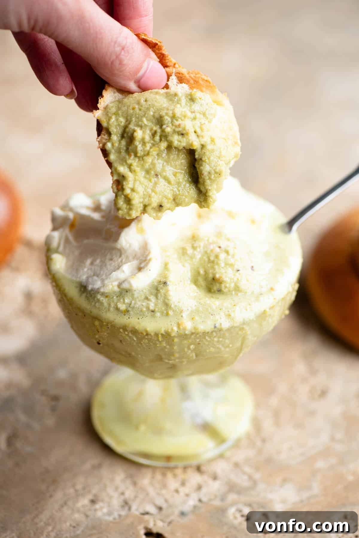 A close-up shot of a golden Sicilian brioche bun being gracefully dipped into a refreshing glass of vibrant green pistachio granita, highlighting the traditional way to enjoy this Italian delicacy.