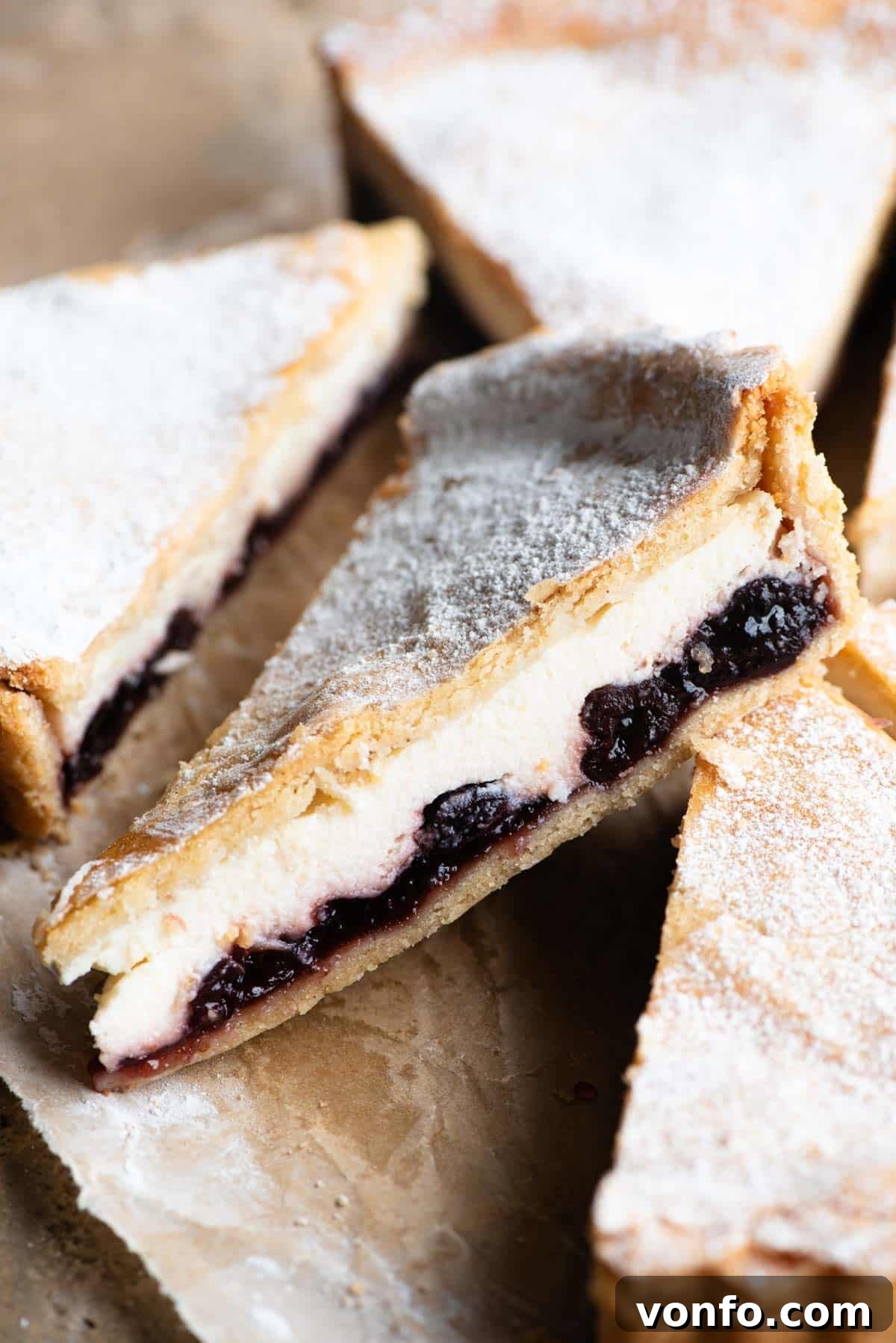 A close up of a slice of ricotta and cherry crostata dusted with powdered sugar, showcasing its golden crust and creamy, fruit-filled interior.