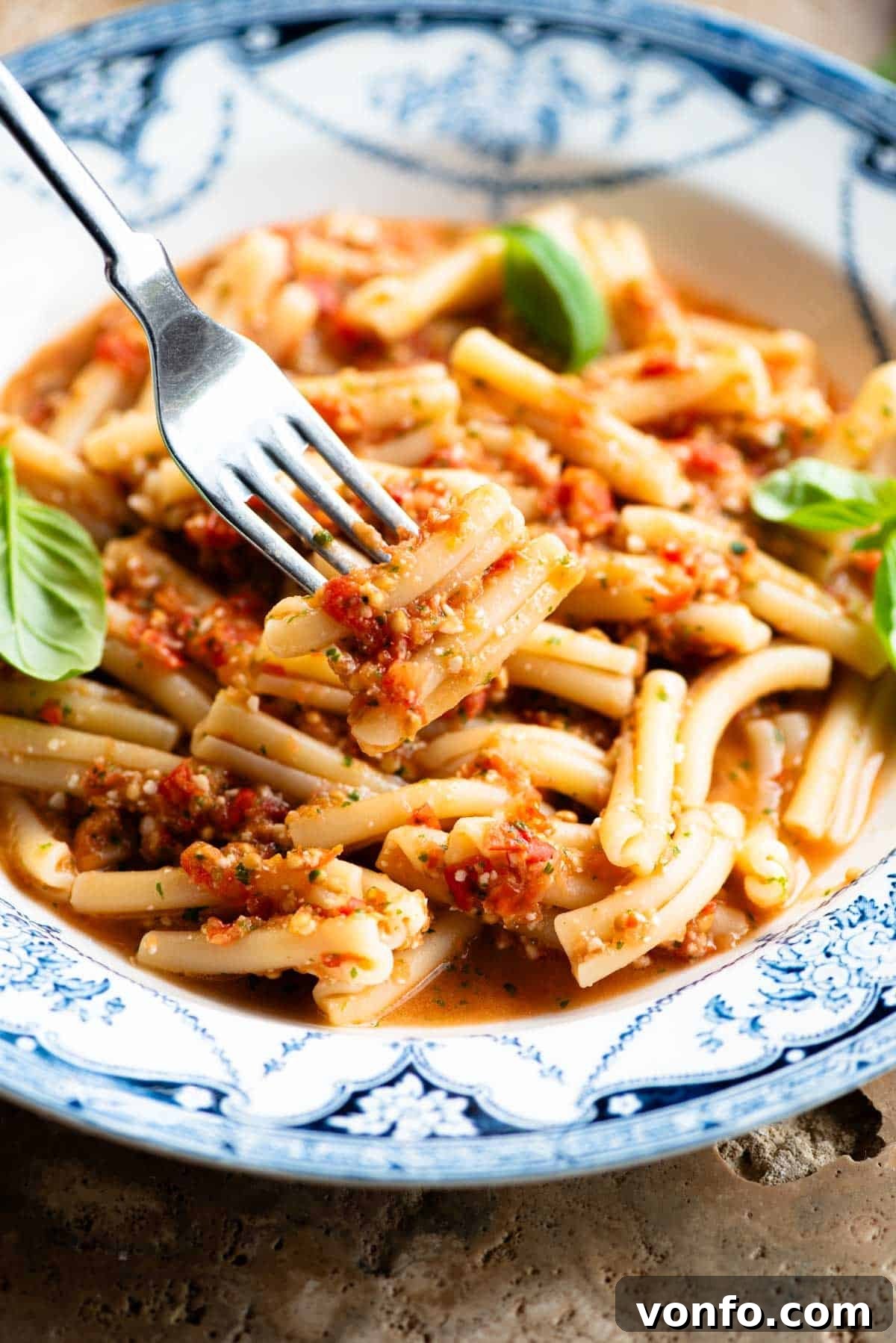 Effortless Fresh Tomato Pasta Sauce 5 A close-up shot of a fork twirling and lifting some pasta with the fresh no-cook tomato sauce, showcasing the vibrant colors and appealing texture, all nestled within a charming blue and white bowl.