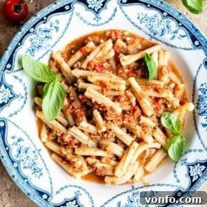 A cropped square image of vibrant pasta with fresh tomato sauce, served in a charming blue and white vintage-style bowl.