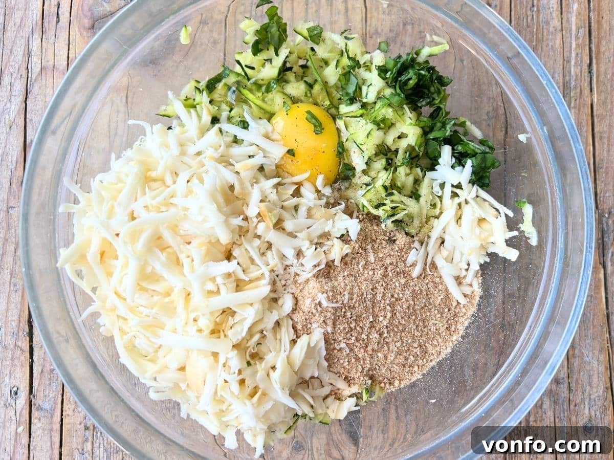 All ingredients for the zucchini patties, including egg, zucchini, breadcrumbs, cheeses, nutmeg, garlic, and basil, in a large mixing bowl.