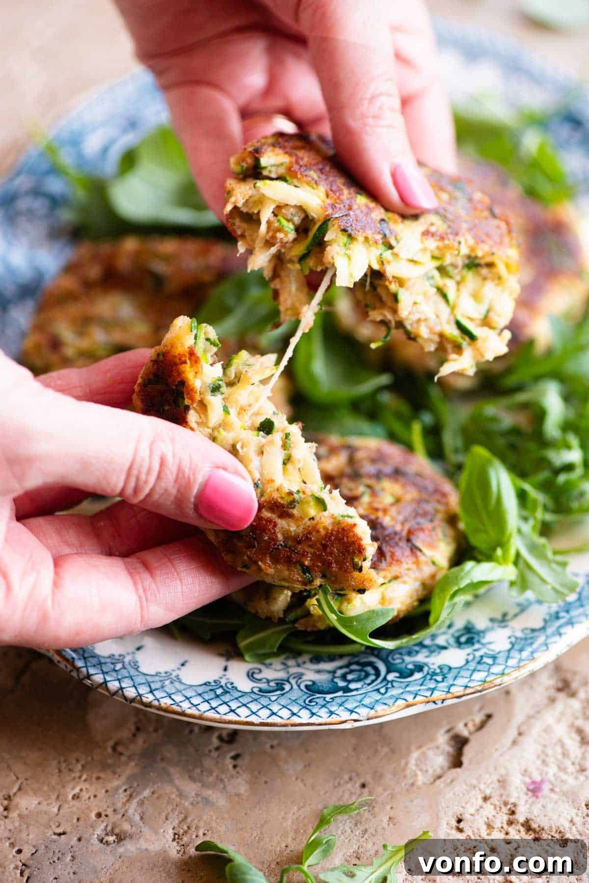 Crispy Zucchini Fritters with Smoked Scamorza 4 Two hands gently pulling a hot zucchini patty in half, revealing the melted, stretchy cheese within the soft, flavorful middle.