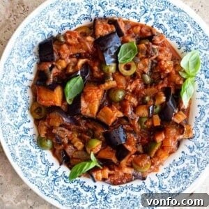 A close up of Sicilian eggplant caponata in a blue and white bowl with basil on top.