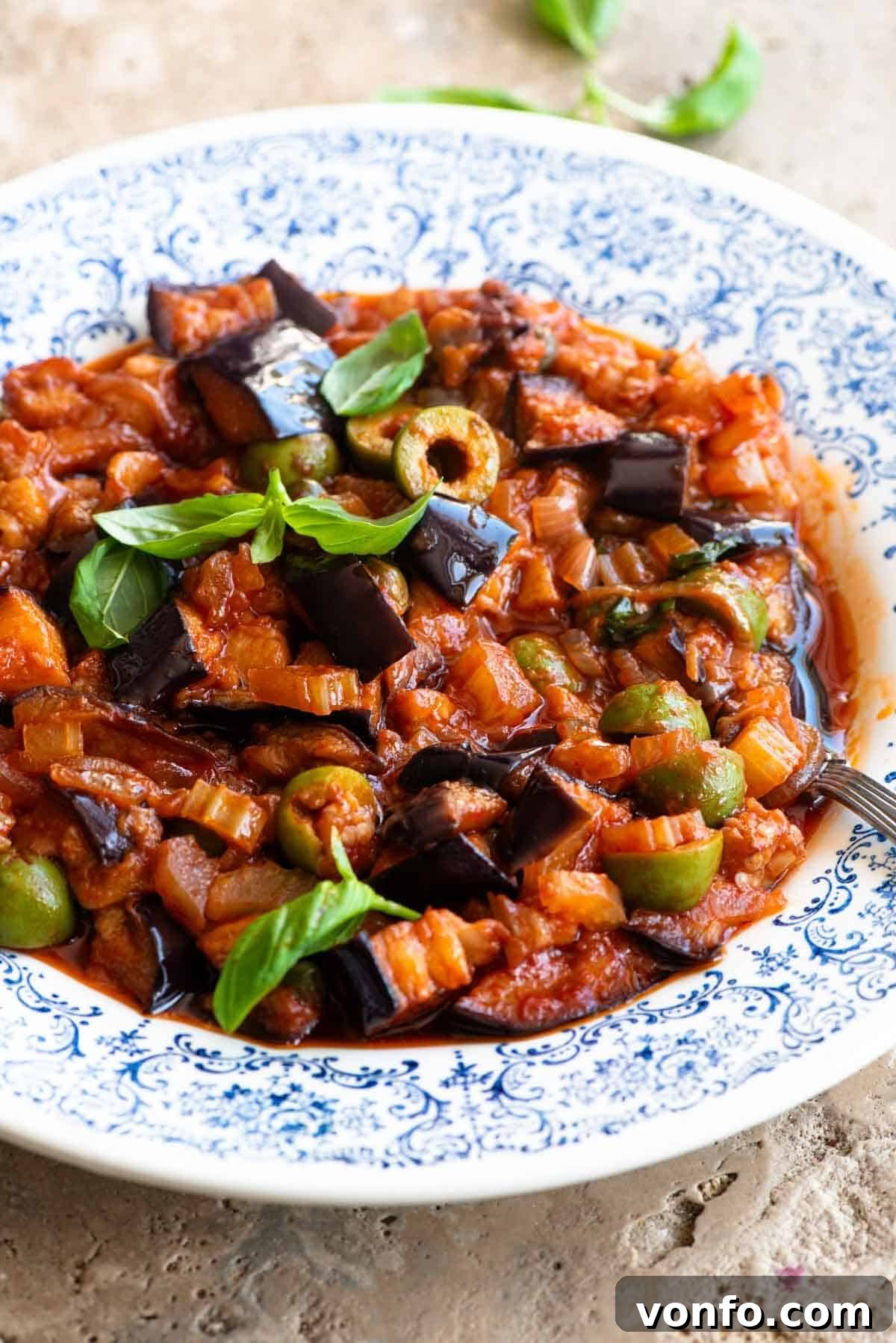 Sicilian Sunshine Caponata 7 A side shot of caponata in a blue and white bowl topped with fresh basil leaves.