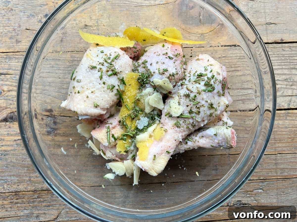 Rustic Tuscan Fried Chicken 6 Chicken thighs and drumsticks marinating in a glass bowl with lemon zest, rosemary, and garlic, resting on a rustic wooden surface.