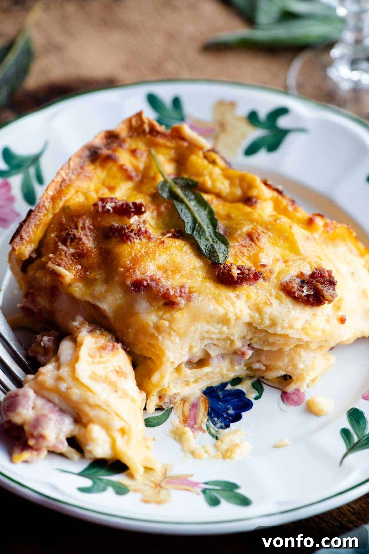 A perfectly portioned, inviting slice of butternut squash lasagna on a floral patterned plate, showcasing the distinct, tender layers of pasta, creamy orange squash béchamel, and savory Italian sausage. The top is golden and slightly bubbly.