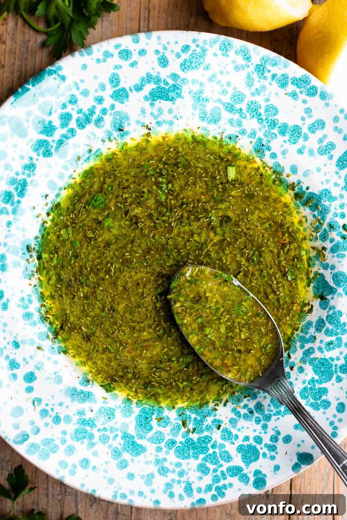 Salmoriglio sauce in a beautiful green splatter pattern bowl, with a spoon resting inside, ready to be served.