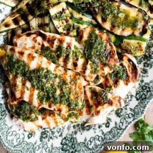 A close up of grilled chicken and vegetables on a plate, beautifully topped with Salmoriglio herb sauce.