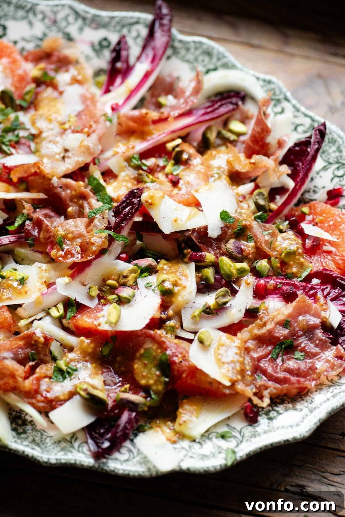 A side shot of a festive salad with blood orange, radicchio, crispy prosciutto, pecorino cheese, pomegranate, and pistachios, showcasing its layers and vibrant colors.