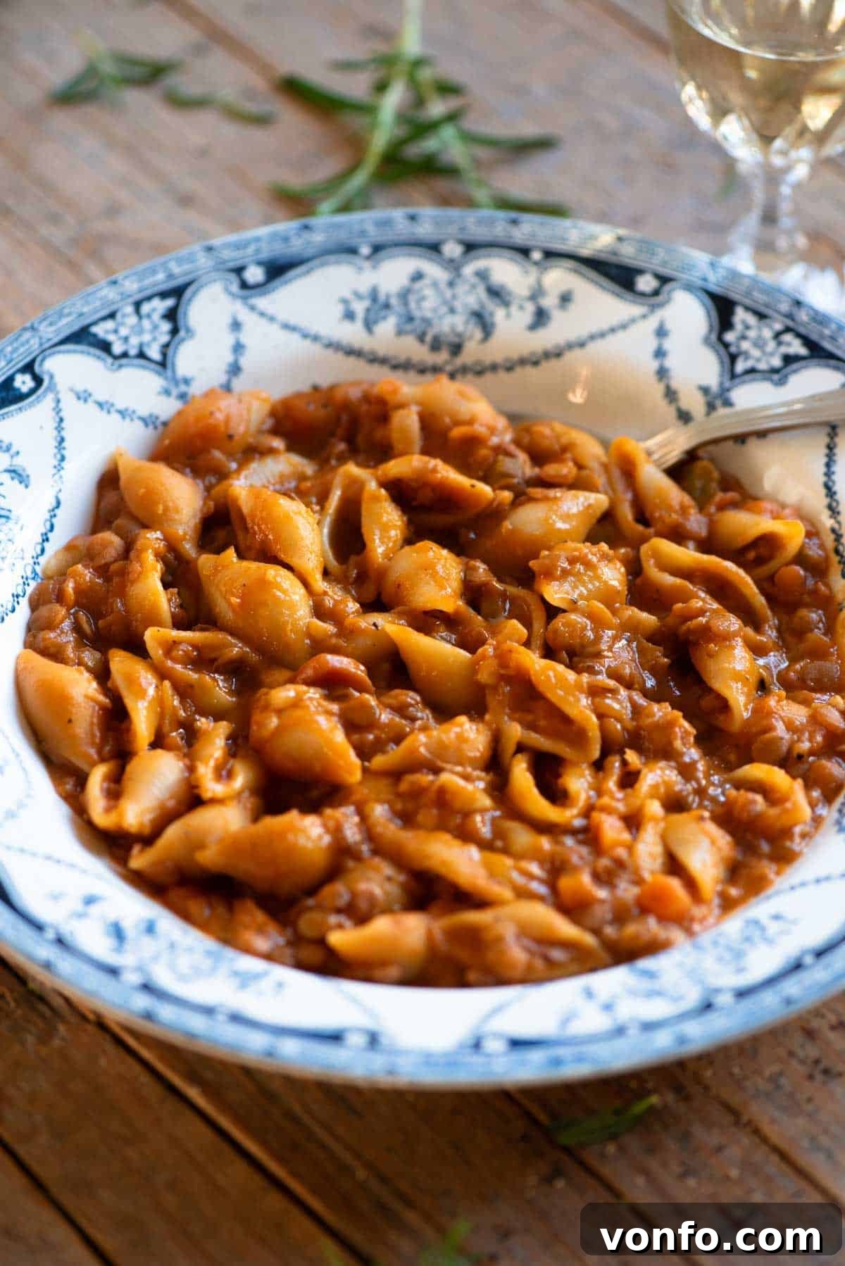 A close-up shot of the perfectly cooked Pasta e Lenticchie, showcasing the small pasta shells and tender green lentils, presented in a charming blue vintage-style bowl with a spoon resting beside it.