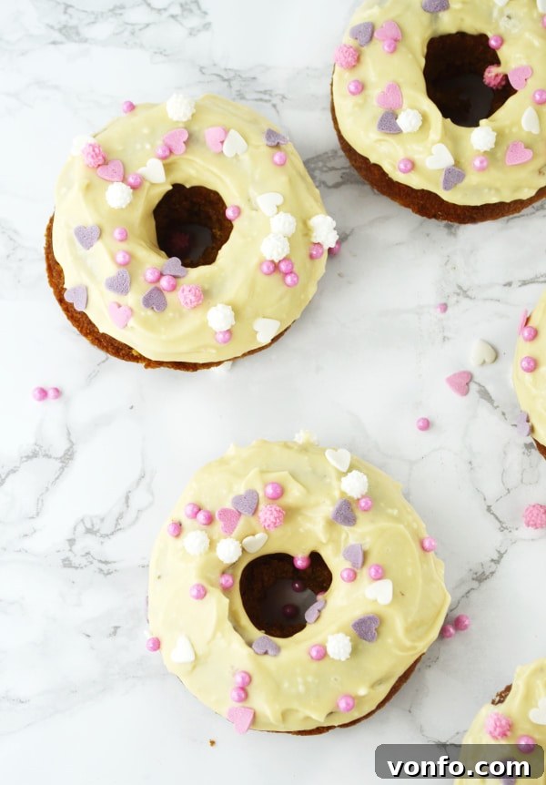 Close-up of a single baked carrot cake doughnut, half-eaten, showing the moist interior and maple frosting. www.insidetherustickitchen.com