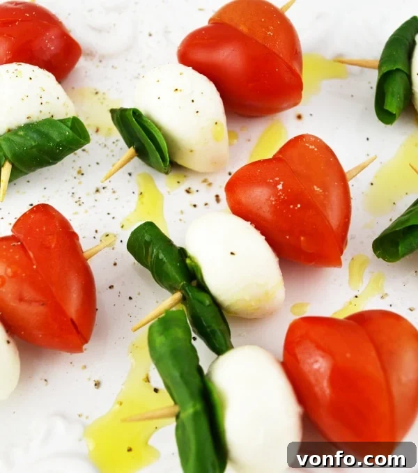 A plate of freshly prepared Valentine's Caprese Skewers, showcasing the vibrant colors of red tomatoes, white mozzarella, and green basil. Drizzled with olive oil.
