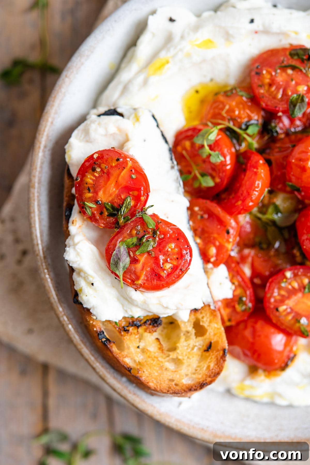 A close-up of a slice of ciabatta bread generously topped with whipped ricotta and sweet roasted tomatoes