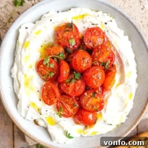A square image of a ricotta dip in a bowl topped with tomatoes