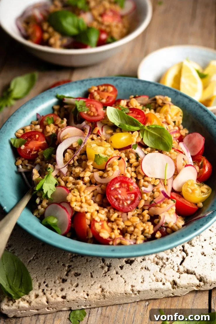 A close-up of a vibrant farro salad in a blue bowl, garnished with fresh basil leaves and halved cherry tomatoes, highlighting its fresh ingredients and inviting texture.