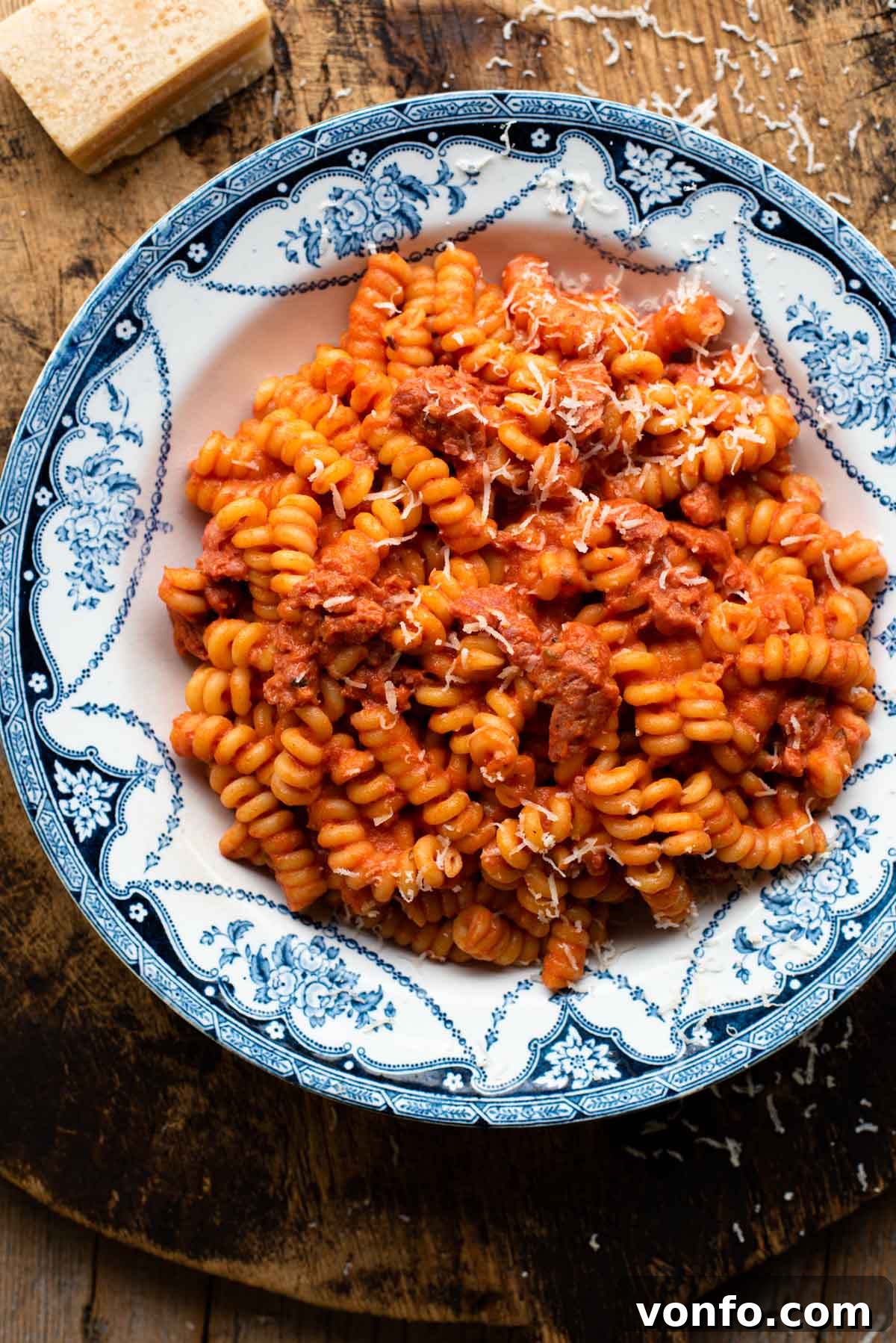 Velvety Tomato Pasta with Hearty Italian Sausage 2 Creamy tomato pasta with sausage in a blue patterned bowl on a wooden serving board, garnished with fresh basil.