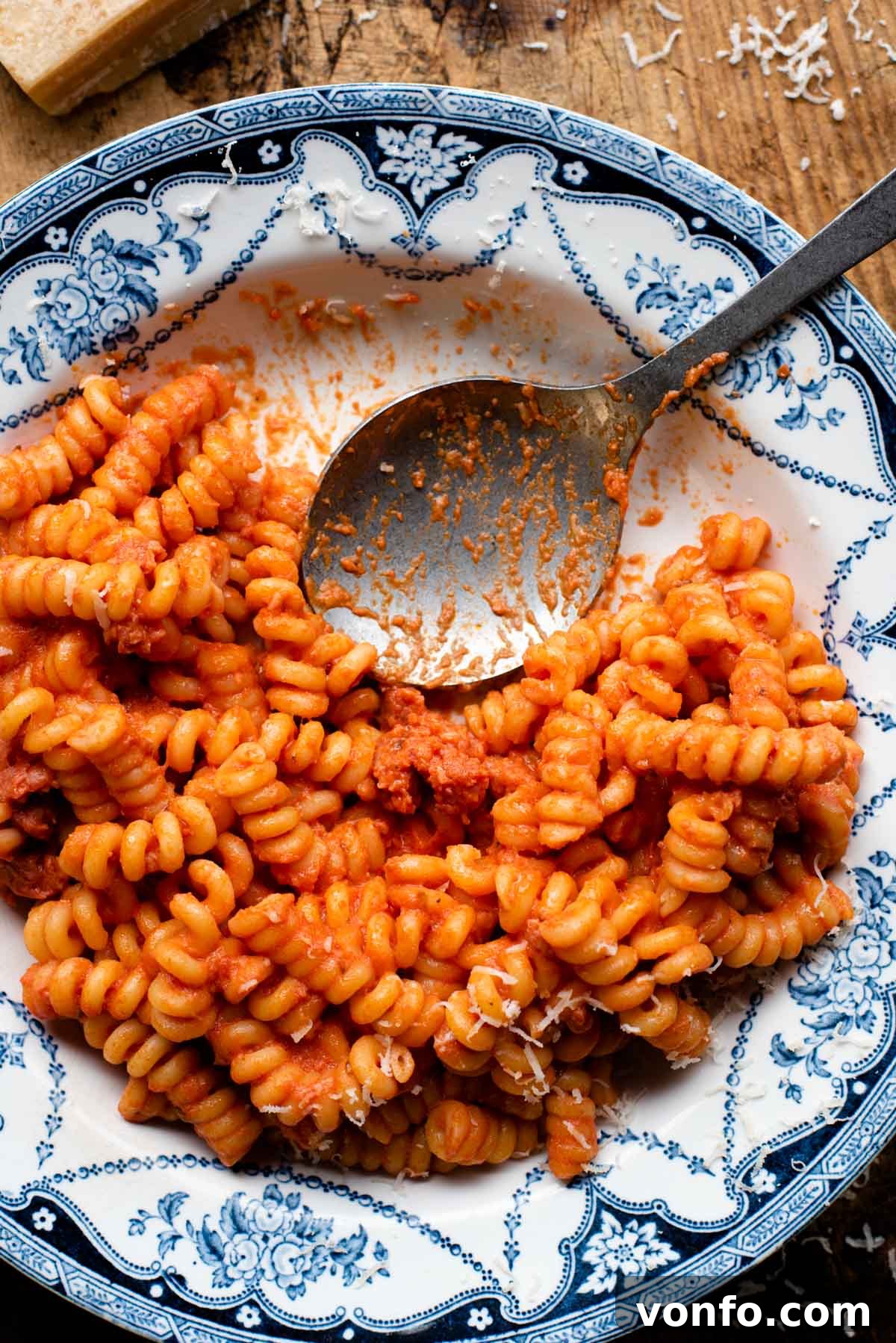 Velvety Tomato Pasta with Hearty Italian Sausage 6 An overhead shot of creamy tomato pasta with Italian sausage in a blue patterned bowl with a serving spoon at the side, ready to be enjoyed.