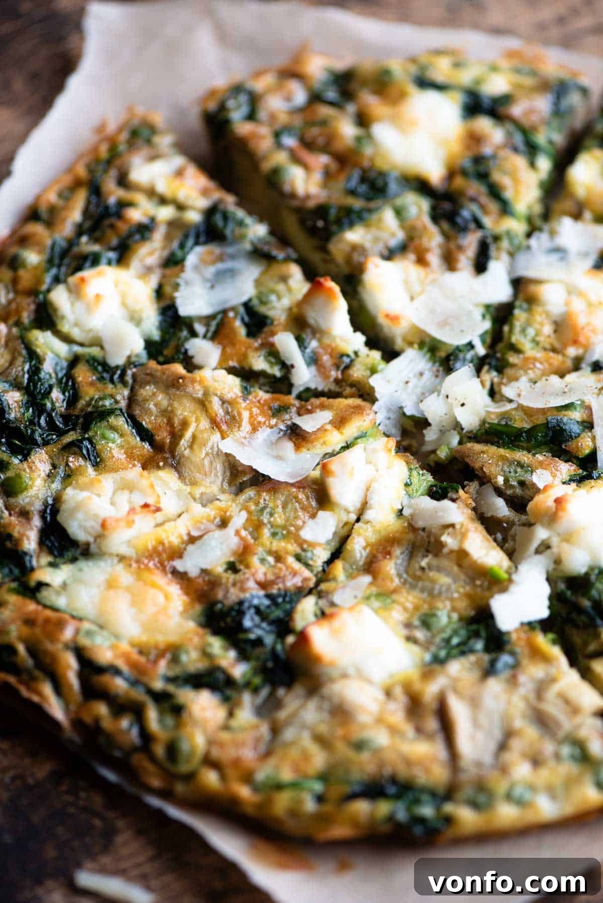 Vibrant Spinach Artichoke Frittata 8 A close-up shot of a freshly baked spinach and artichoke frittata, garnished with extra shavings of Pecorino and delicate goat's cheese, cut into perfect, inviting slices.