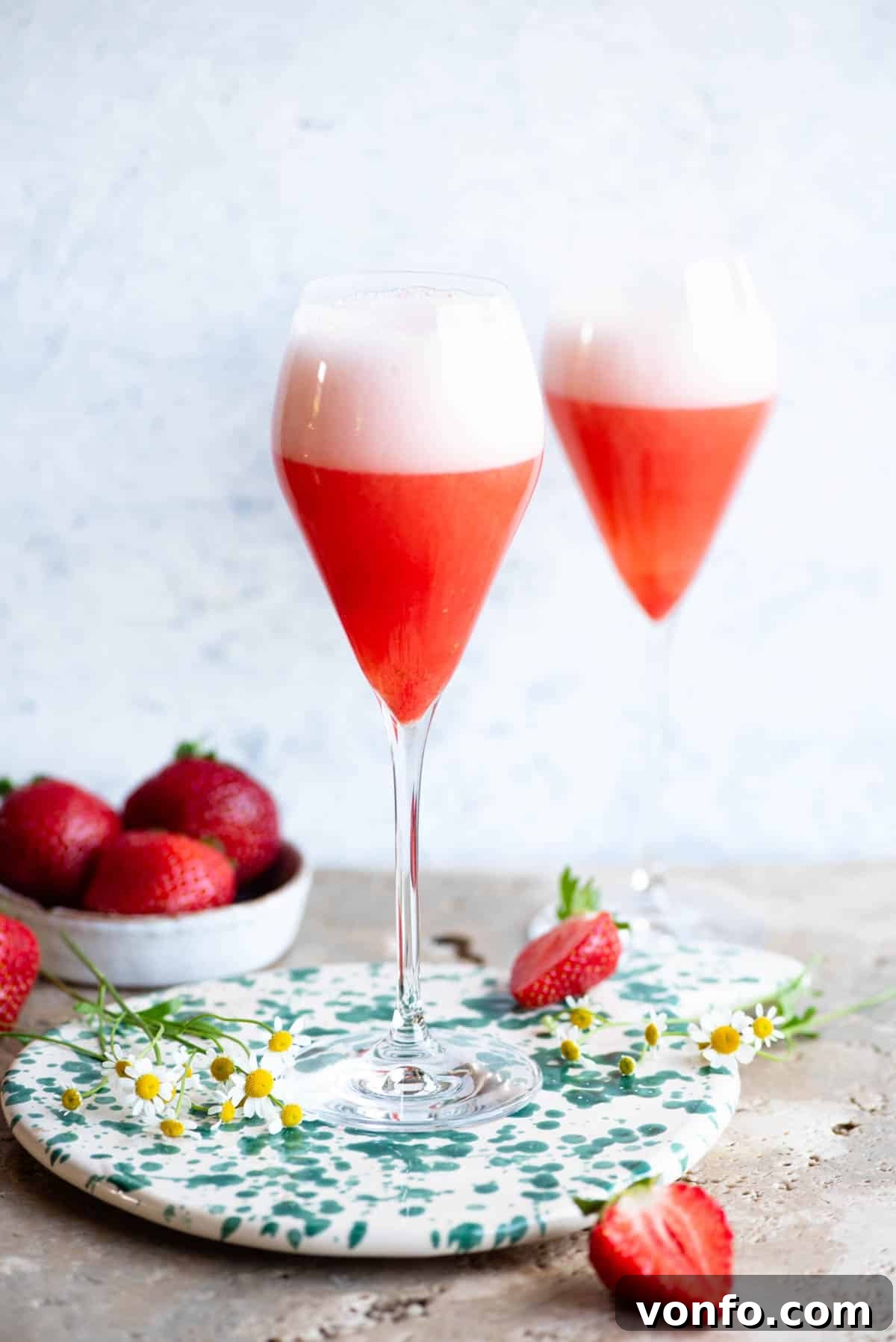 Strawberry Blush Sparkler 4 Two elegant flute glasses brimming with vibrant Rossini cocktails, set on a chic stone counter against a soft light blue background, ready for enjoyment.