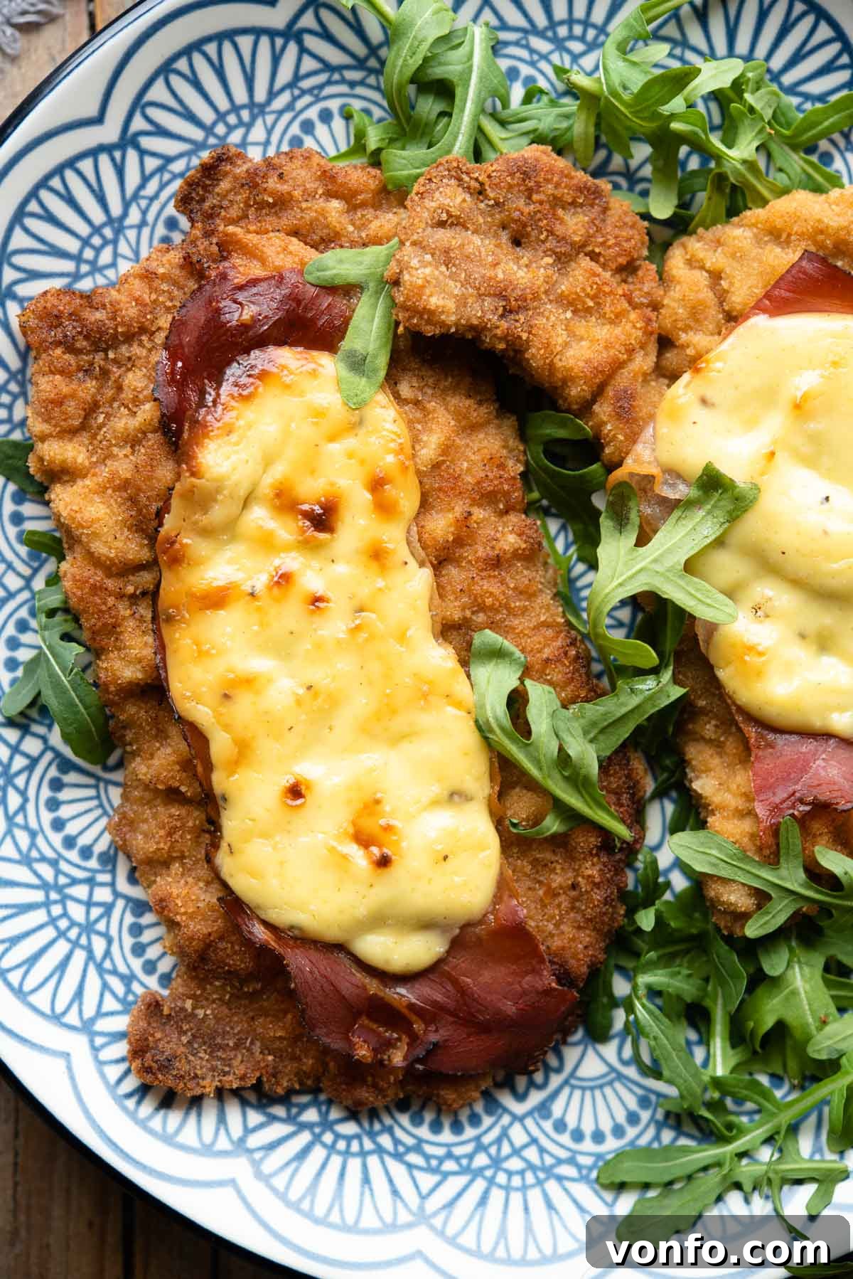 An overhead shot of breaded veal cutlets on a plate topped with parmesan cream and prosciutto
