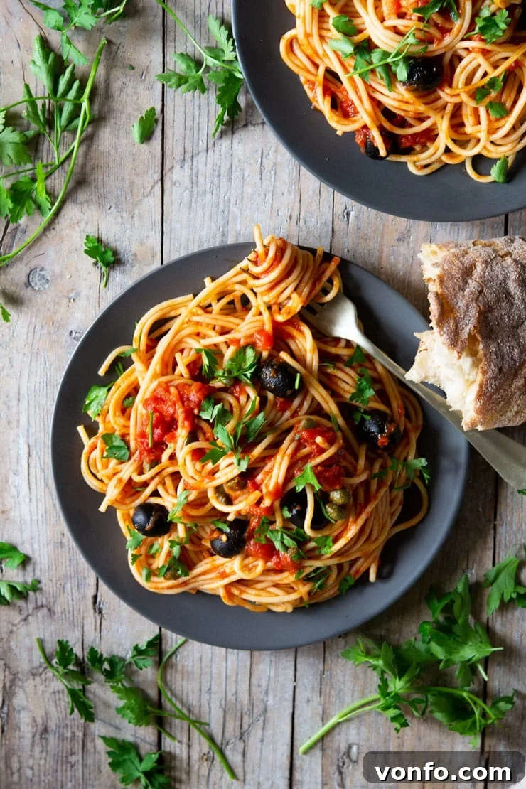 A fantastic Spaghetti alla Puttanesca recipe using fresh cherry tomatoes, capers, olives and garlic it's packed full of flavour and ready in minutes! insidetherustickitchen.com An overhead shot of a plate of spaghetti with puttanesca sauce and chopped parsley scattered around