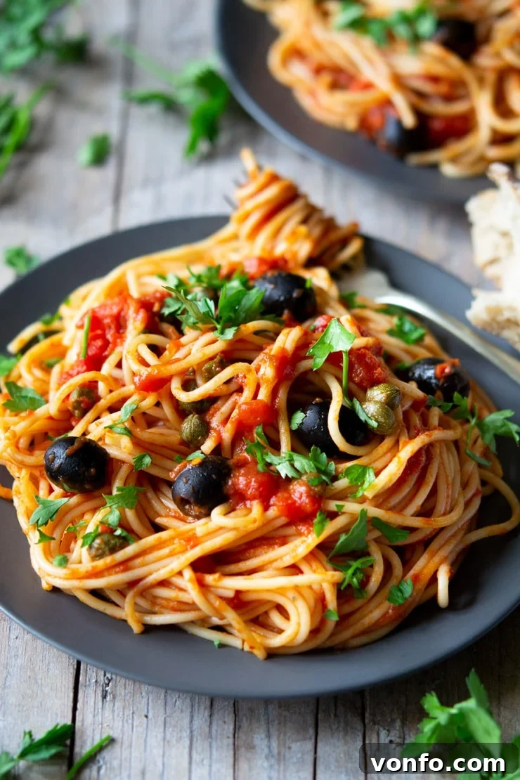 A fantastic Spaghetti alla Puttanesca recipe using fresh cherry tomatoes, capers, olives and garlic it's packed full of flavour and ready in minutes! insidetherustickitchen.com A close up of spaghetti on a plate with puttanesca sauce sitting on a wooden surface