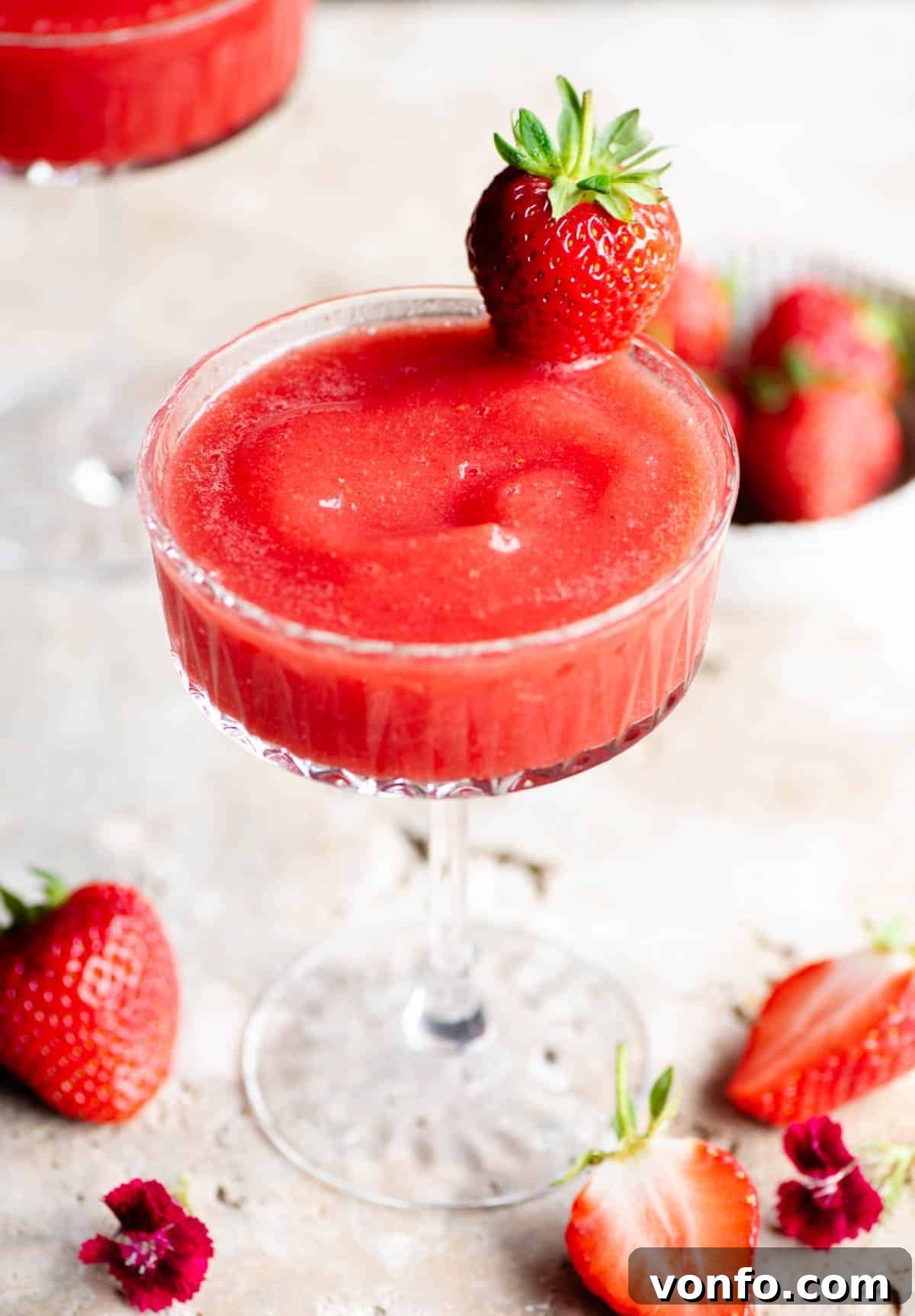 Velvet Strawberry Prosecco 3 A close up of a frozen strawberry cocktail in a delicate cocktail glass, elegantly garnished with a whole fresh strawberry on the rim.