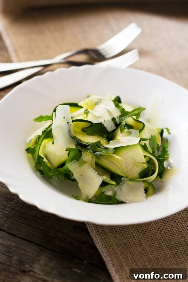 A bowl of Zucchini Ribbon Salad with lemon dressing, arugula, and parmesan, garnished with basil leaves, ready to be enjoyed. A delightful and healthy summer meal from insidetherustickitchen.com