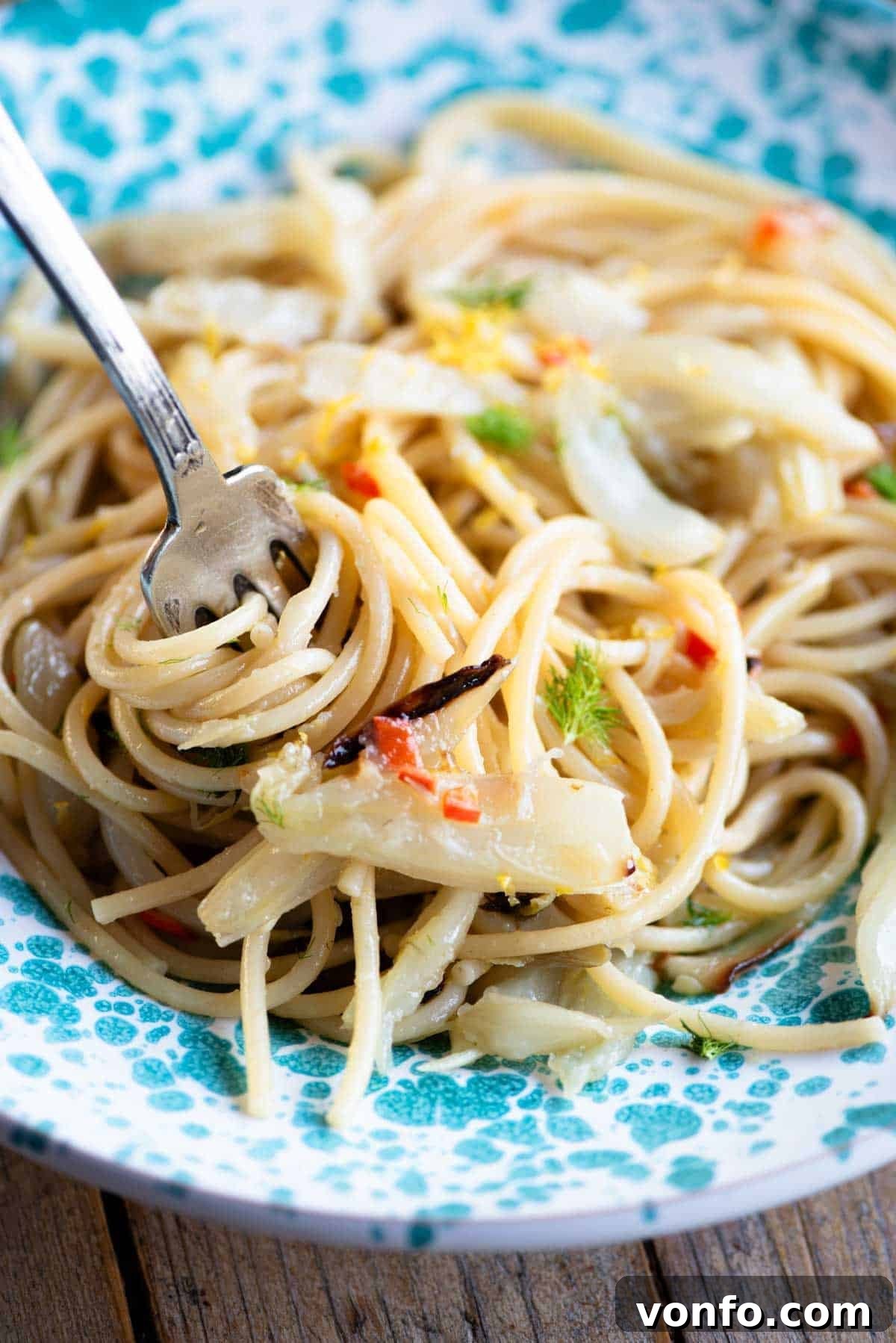 A close up of roasted fennel spaghetti in a bowl twirled around a fork, showing the vibrant colors of chili, lemon zest, and fennel.