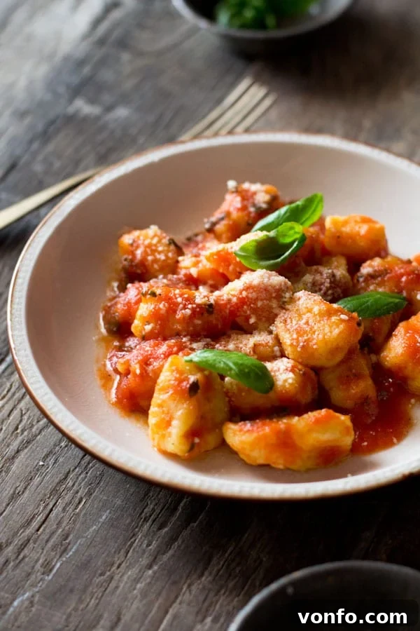 Light and soft gnocchi with fresh tomato sauce recipe with ripe tomatoes, oregano, and garlic. Simple, easy, and authentic Italian tomato sauce for gnocchi and pasta. Close-up of gnocchi with fresh tomato sauce in a white bowl, garnished with a sprinkle of fresh parmesan
