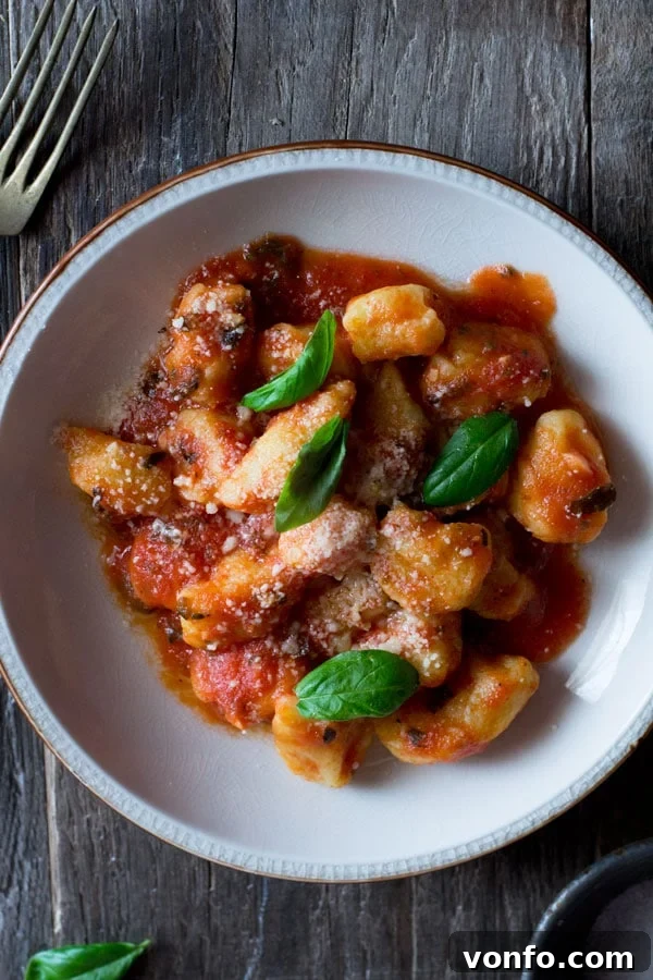 Light and soft gnocchi with fresh tomato sauce recipe with ripe tomatoes, oregano, and garlic. Simple, easy, and authentic Italian tomato sauce for gnocchi and pasta. Gnocchi with fresh tomato sauce on a wooden table inside a cozy rustic kitchen, ready to be enjoyed