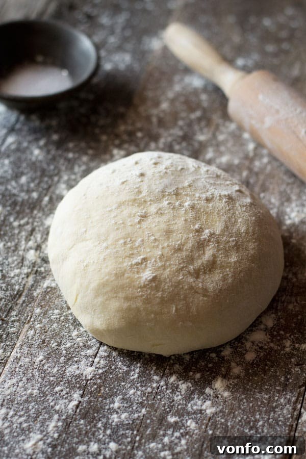 Yeast-free pizza dough on a wooden surface with flour at the side, ready to be rolled out