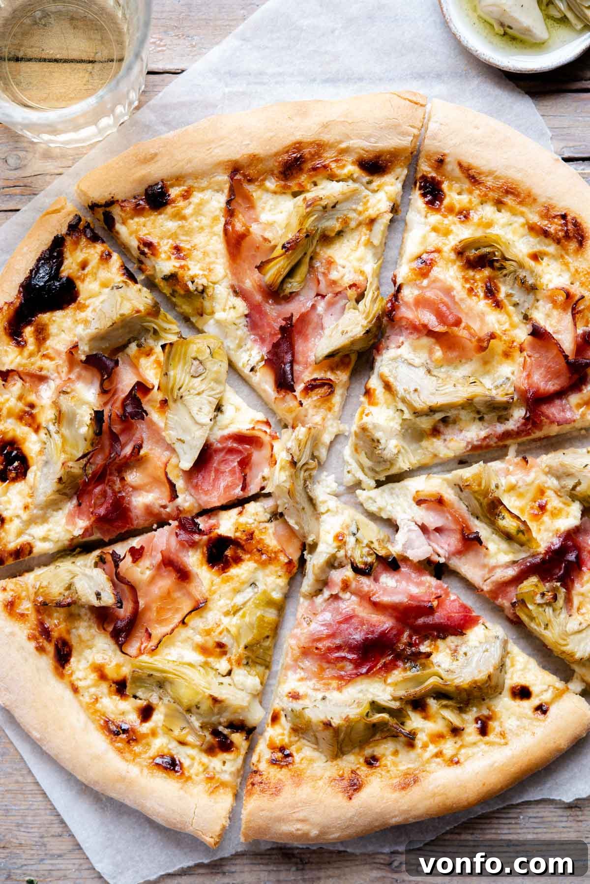 An overhead shot of a freshly baked artichoke pizza, cut into golden slices, showcasing the melted cheese, tender artichokes, and savory prosciutto on a crispy crust.