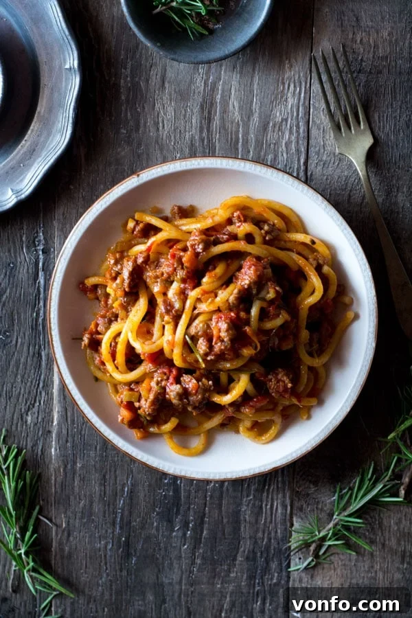 Authentic Tuscan Sausage Ragu with Pici Pasta, made with premium Italian sausages, fennel, red wine, and garlic for an unforgettable meal. Discover more traditional Italian pasta recipes and authentic Italian cuisine. Rich Tuscan Sausage Ragu with Pici Pasta in a rustic kitchen setting, highlighting the deep colors and texture of the sauce and thick pasta.
