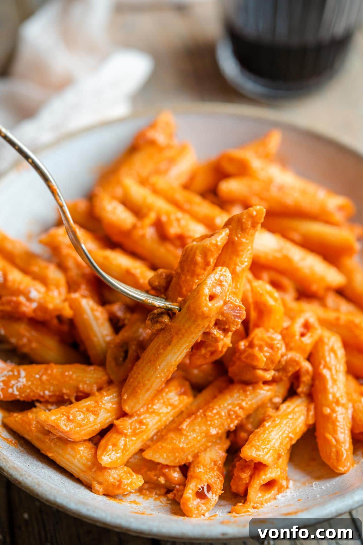 A close up of a fork picking up penne pasta coated in a creamy tomato vodka sauce with bits of pancetta