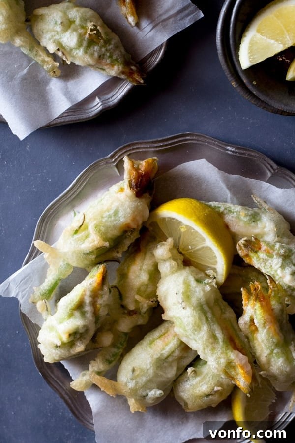 Crispy, deep fried ricotta stuffed zucchini flowers with lemon and chili flakes. An easy, elegant and fun Italian appetizer that's hard to resist. How to fry zucchini flowers and recipe at Inside the rustic kitchen - authentic Italian recipes. Freshly fried ricotta stuffed zucchini flowers cooling on paper towels, ready to be served as an appetizer.