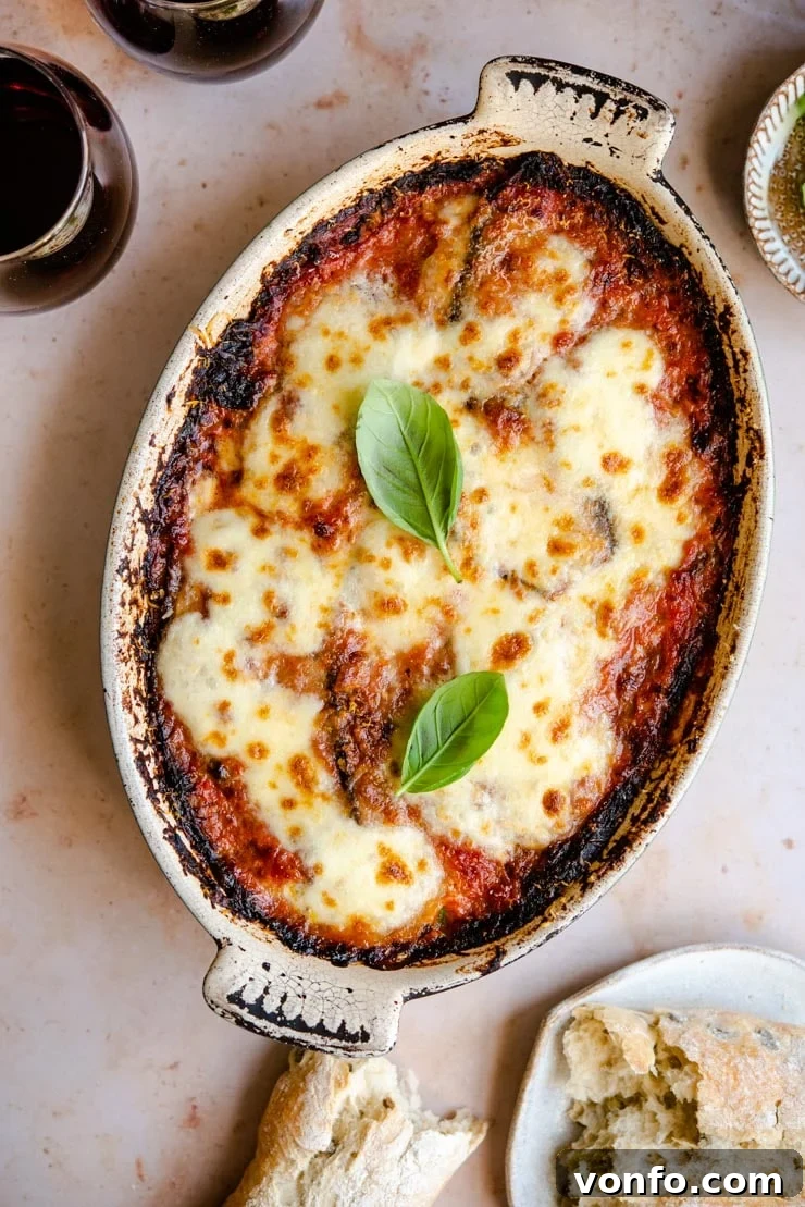 Parmigiana di Melanzane - Eggplant Parmigiana Overhead shot of bubbling golden Eggplant Parmigiana in a rustic serving dish with fresh basil garnish