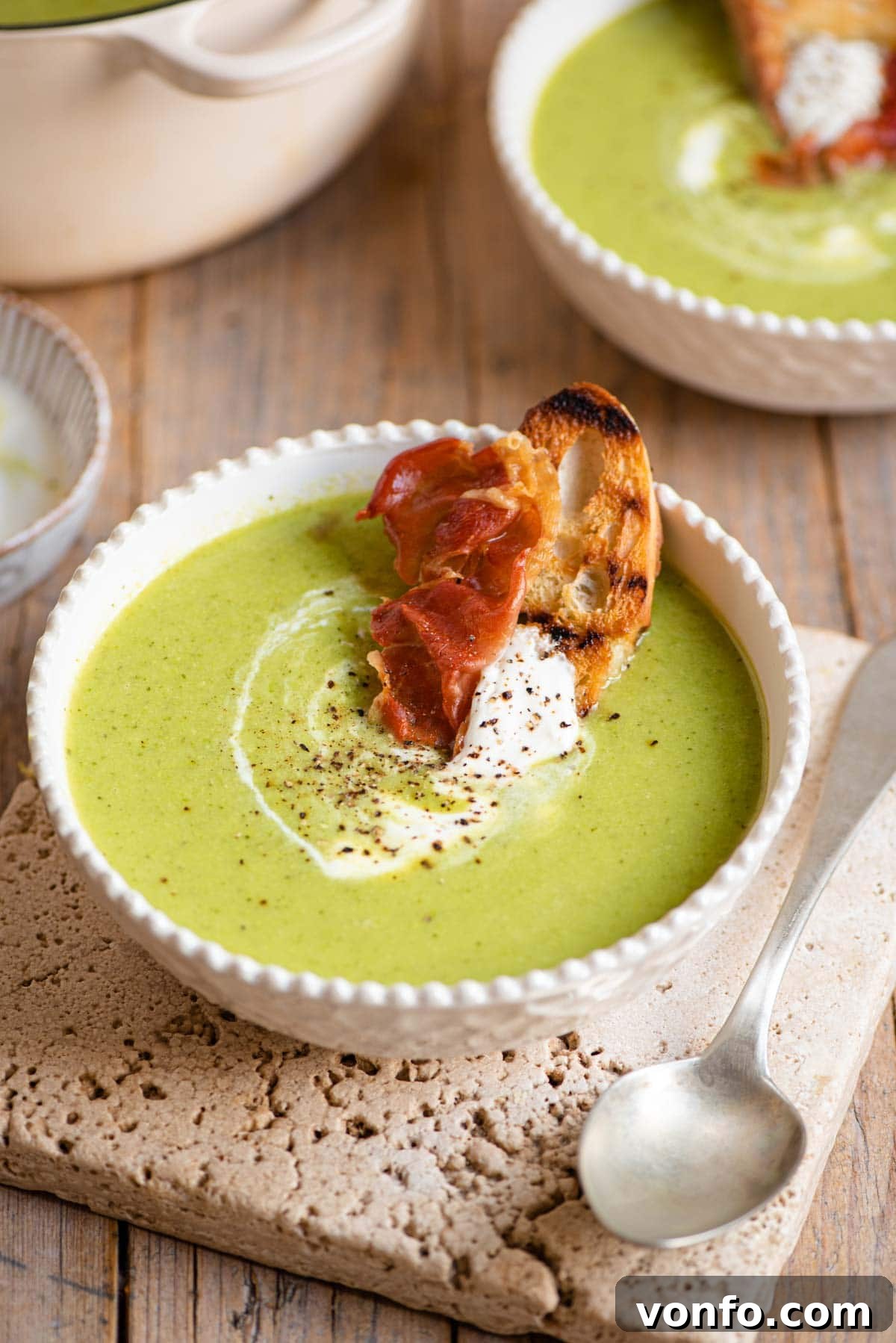 Silky Green Pea Soup with Prosciutto Crisps 2 Green pea soup in a bowl topped with yogurt and crispy prosciutto, ready to be enjoyed.