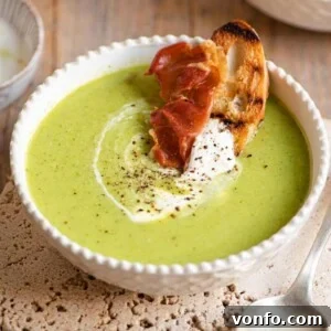 A close up of green pea soup with a slice of bread and prosciutto at the side