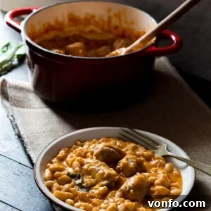 Appetizing Tuscan bean stew with Italian sausages served on a plate, with a fork and the cooking pot blurred in the background.