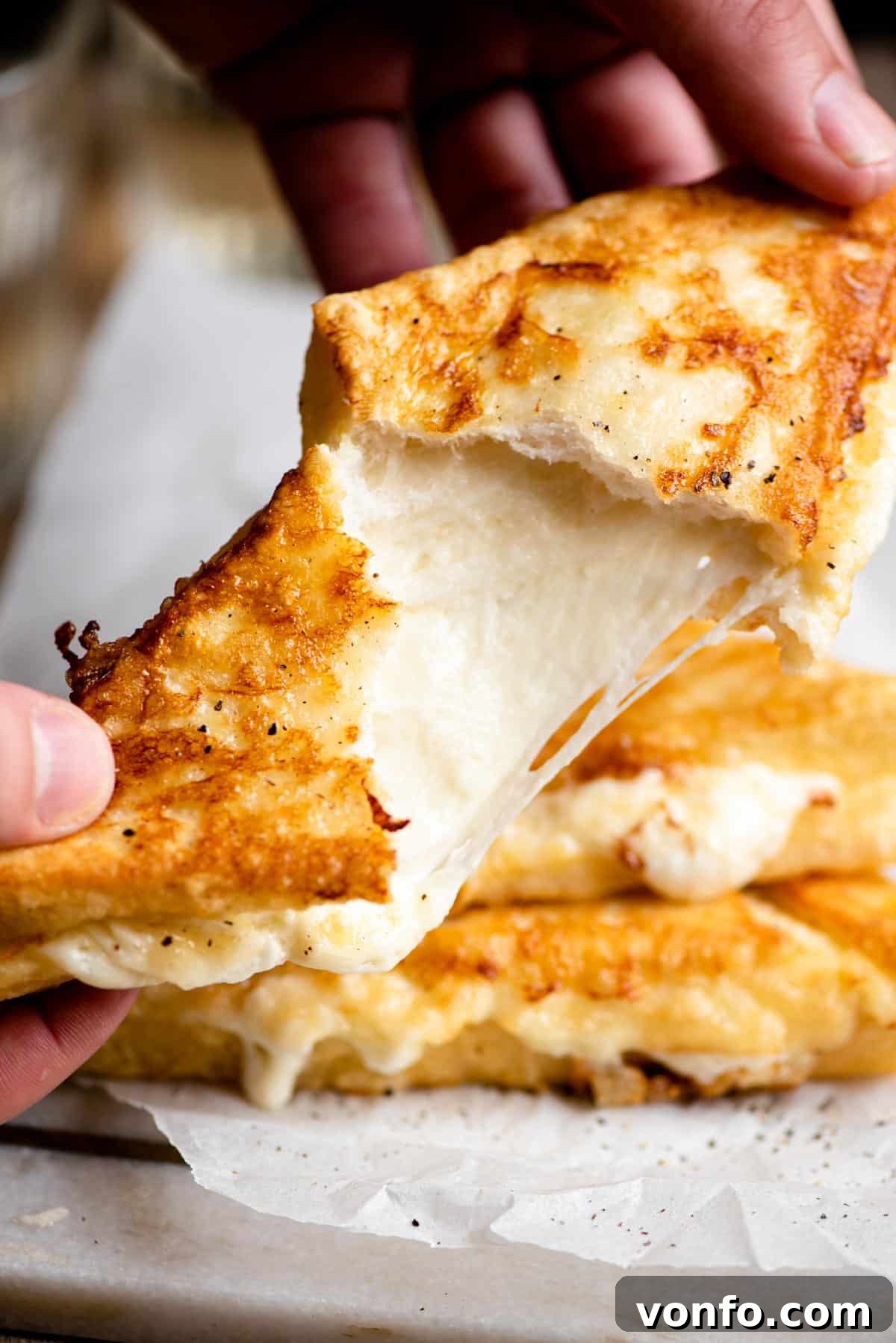 A close up of a fried mozzarella sandwich broken open with cheese oozing and stretching, highlighting the creamy interior